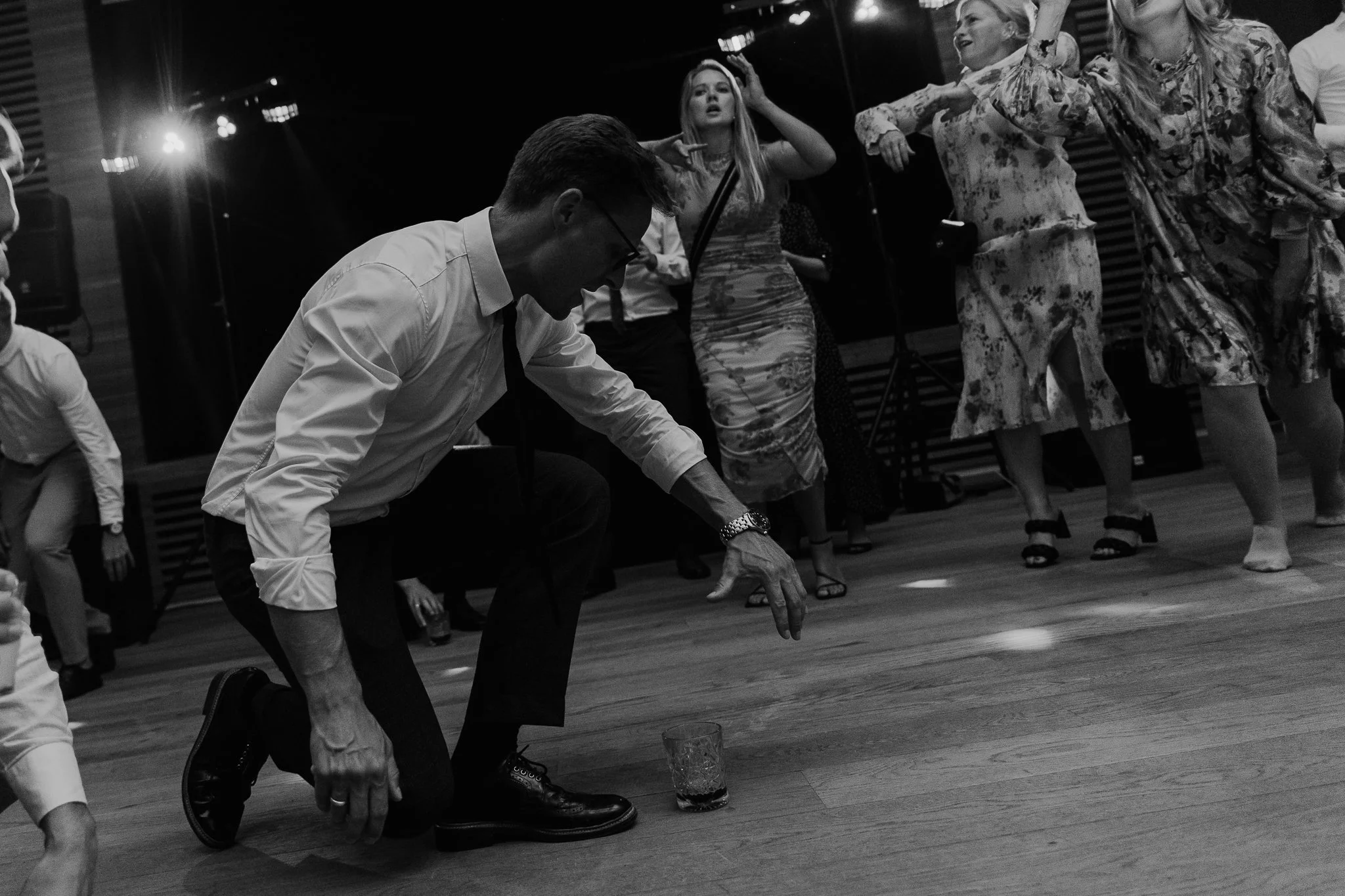 Sort-hvid foto af en gruppe mennesker, der danser og har det sjovt, med en person i forgrunden nedknælende på gulvet.