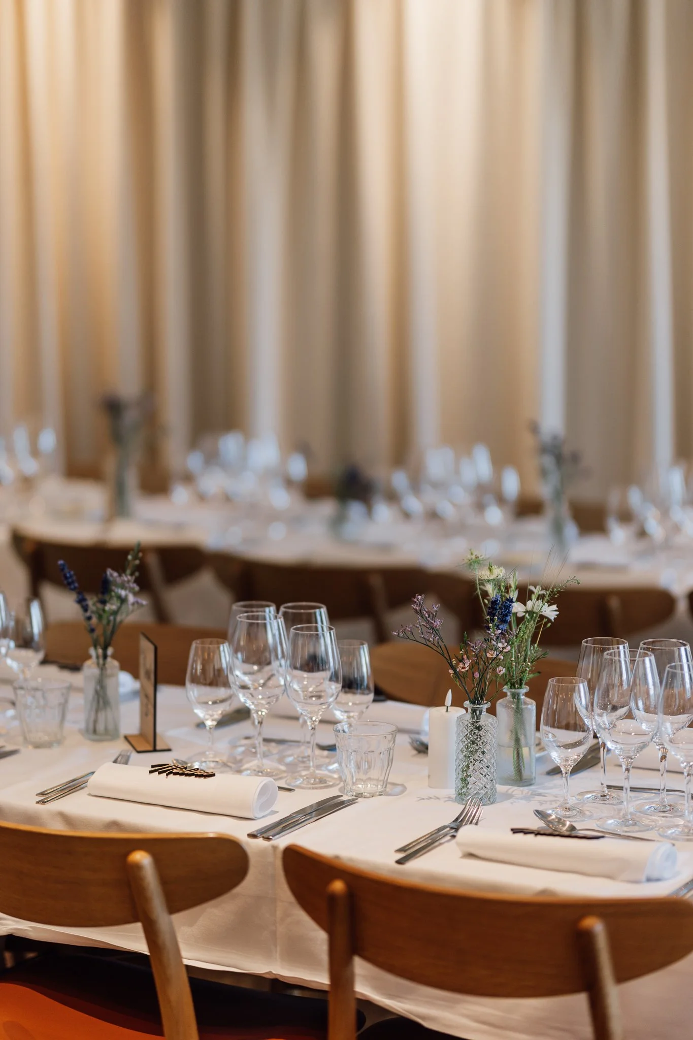 Et spisebord er dækket op til fest med vin, glas, blomsterdekorationer og servietter i en sammenhængende indretning.
