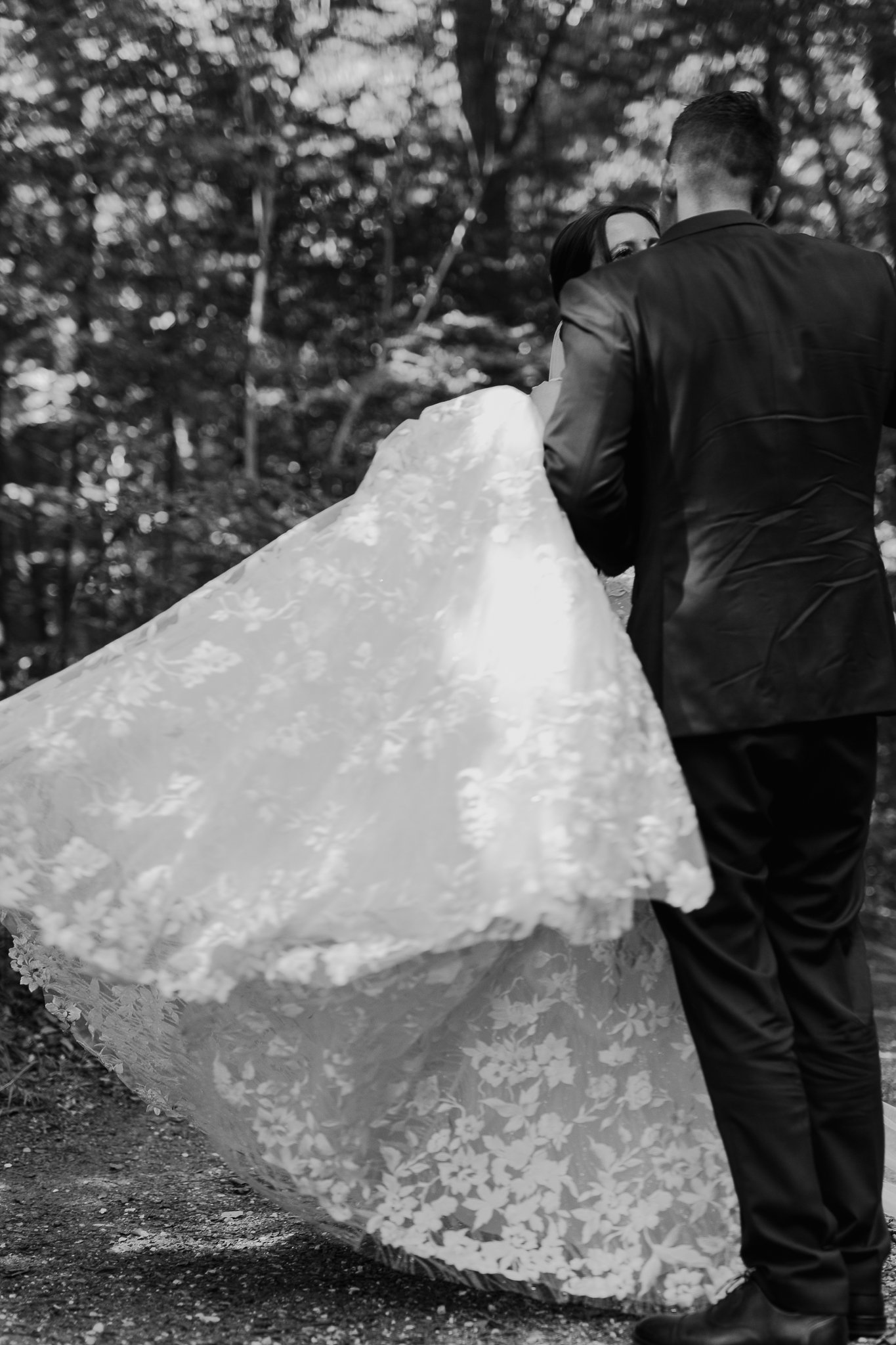 To personer, der står udenfor, hvor den ene person iført sort jakkesæt holder en brudekjole med blomstermønster, som den anden person, der har mørkt hår, bærer.