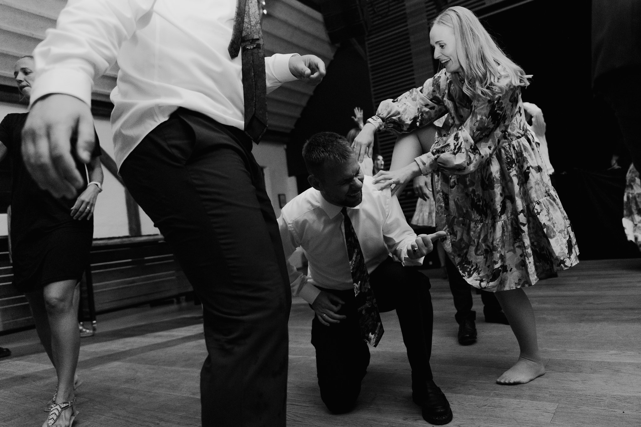 Sort-hvid foto af mennesker, der danser i et rum med træborderskinner i loftet. Den kvindelige danser er iført en blomstrede kjole, og den mandlige danser er klædt i en hvid skjorte og slips, mens de danser. Flere personer kan ses i baggrunden.