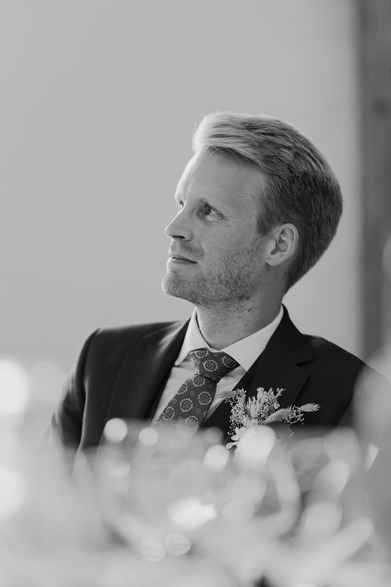 Sort-hvid portrætfoto af en mand i formelt tøj med buket blomster, sidder i en professionel indretning.