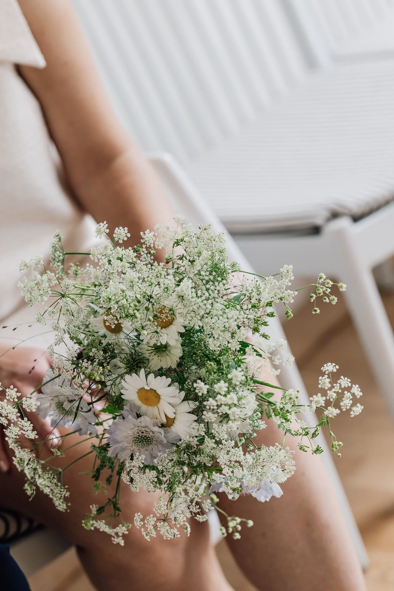 Person holder en buket af hvide og gule blomster, mens de sidder ned.