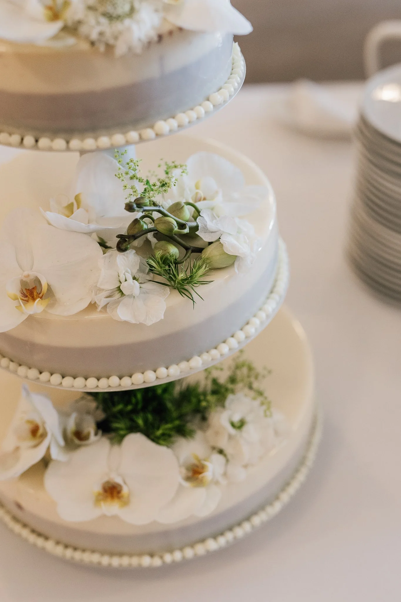 Et flerlags festkage pyntet med hvide blomster og grønne blade, med lagdelte cirkler af blomster rundt om kagen.