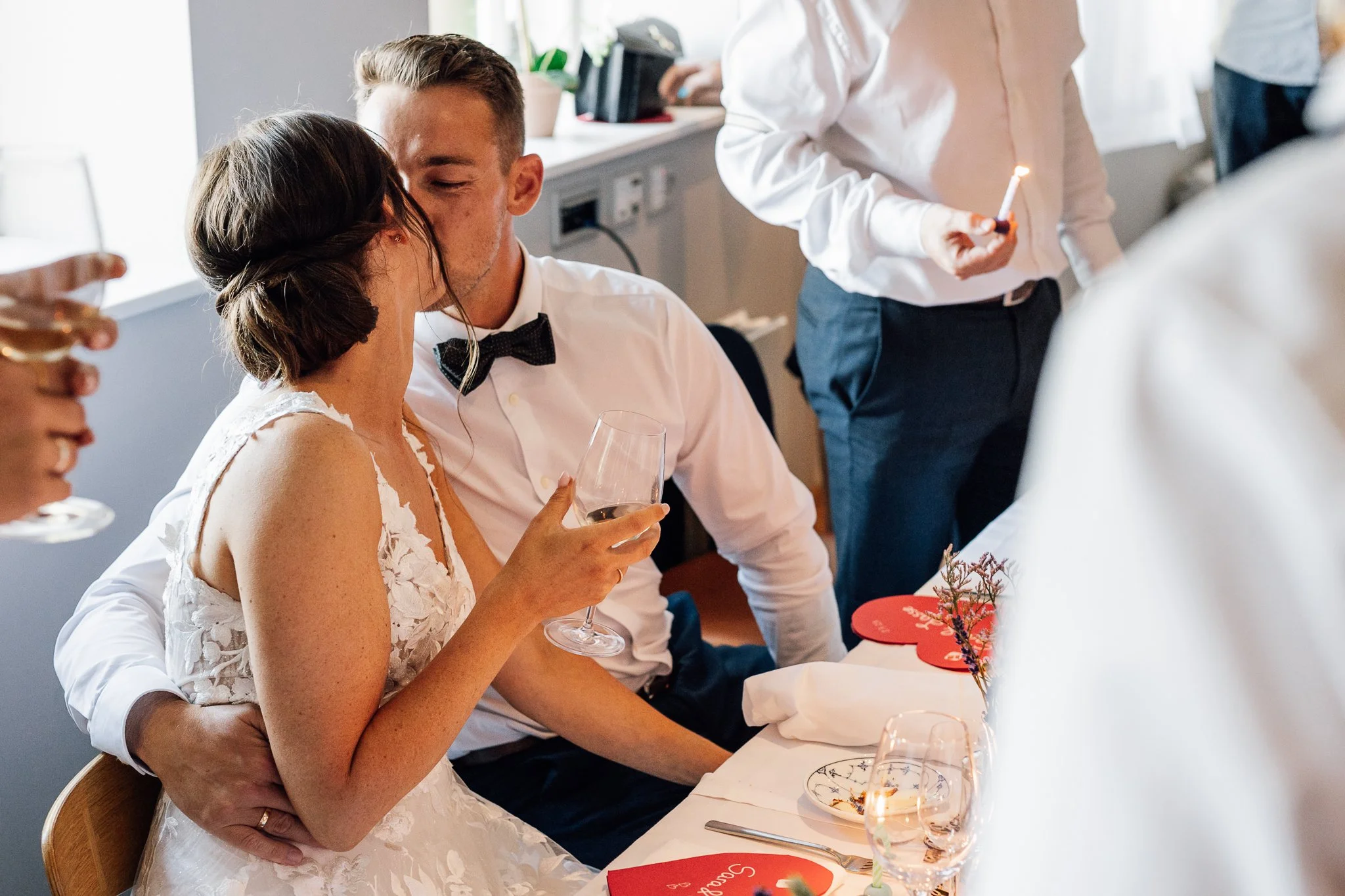 Et bryllupscenarie med en brud, der holder en vaser med blomster, og en mand, der sidder tæt ved hende og holder en vinflaske.