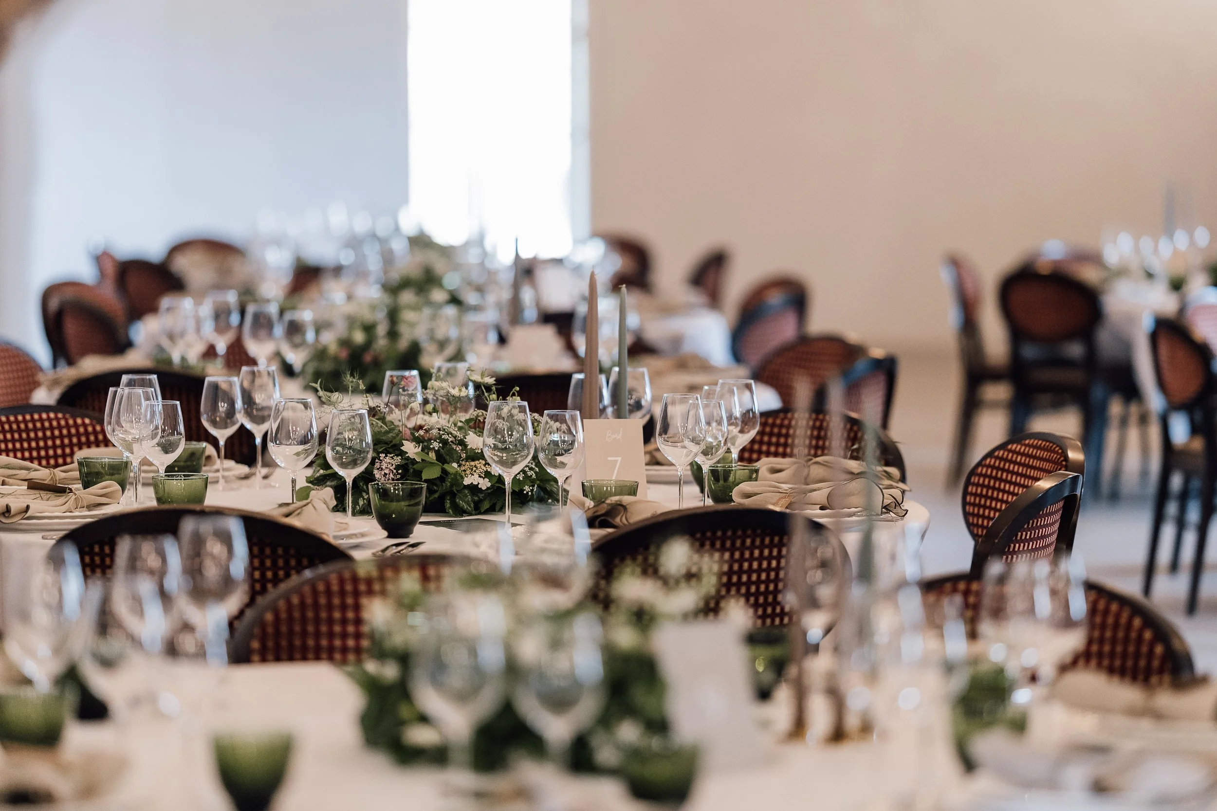 Festbord med blomsterdekorationer, glas, og stearinlys i et festlokale.