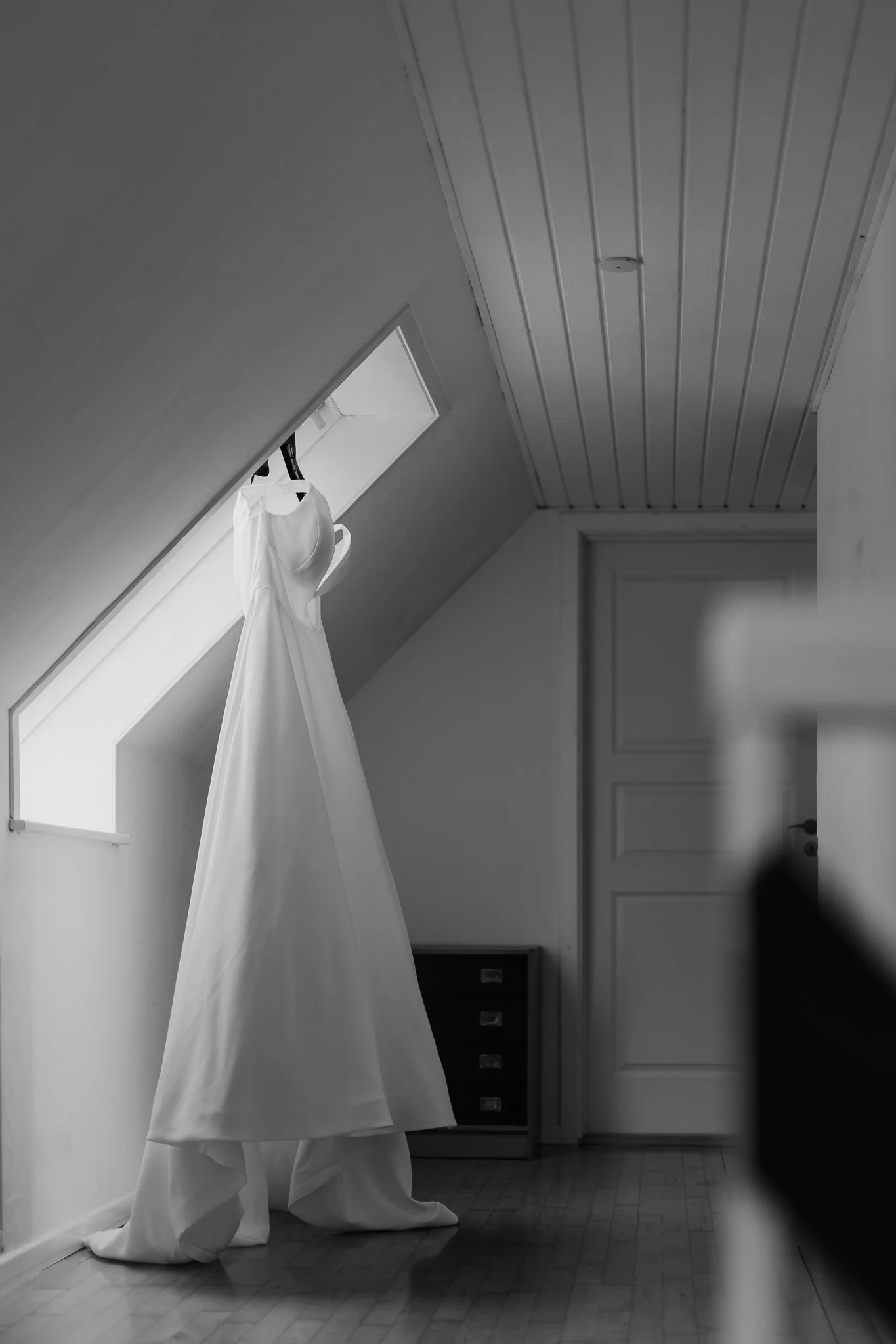 Sort-hvid billede af en væg med et dør og nogle skuffer, et vindue med en hængende hvid kjole.