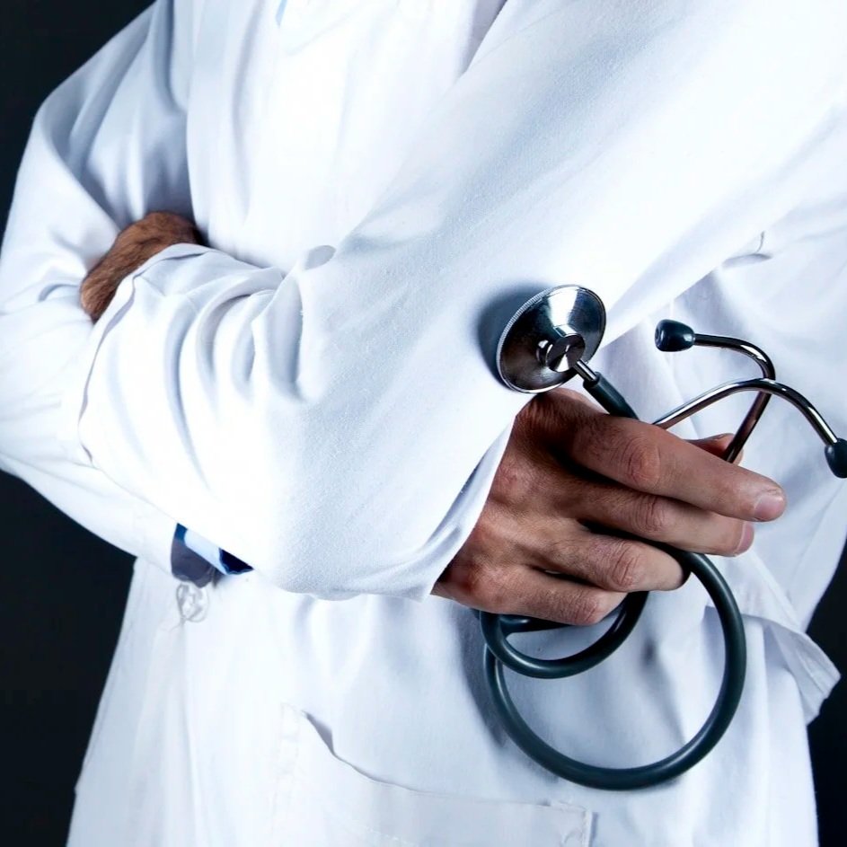 A healthcare professional wearing a white lab coat, holding a stethoscope in their hand with arms crossed.