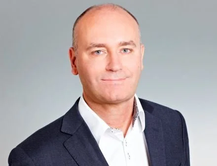 Professional headshot of a man wearing a suit and white shirt against a plain background.