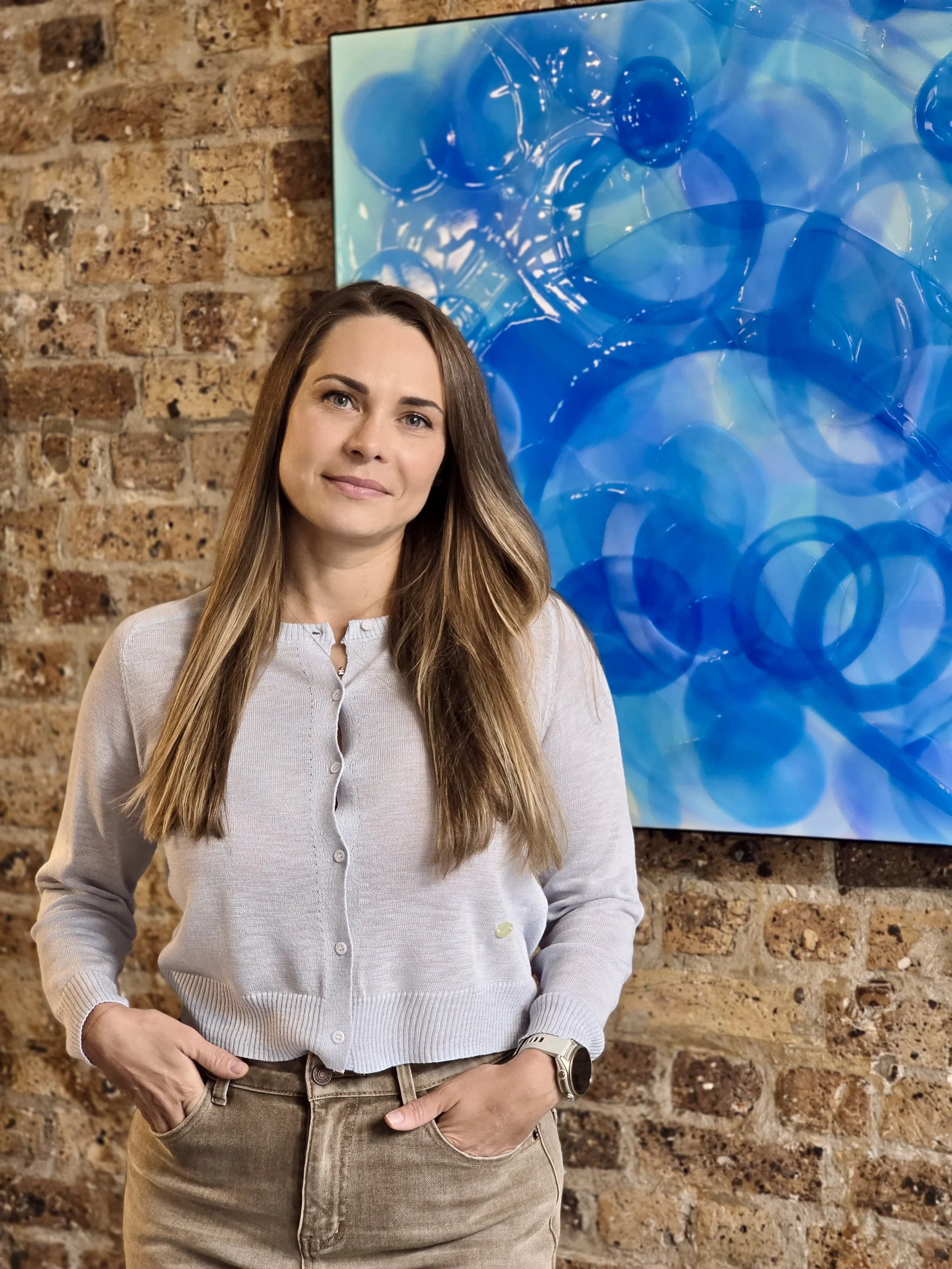 Contemporary fine artist Daria Baluta standing next to her high-gloss multi-layered epoxy resin artwork Cerulean.