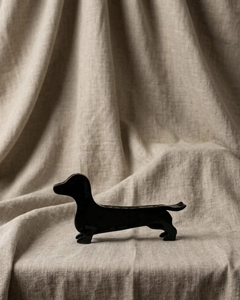 Black dachshund-shaped figurine placed on beige fabric background.