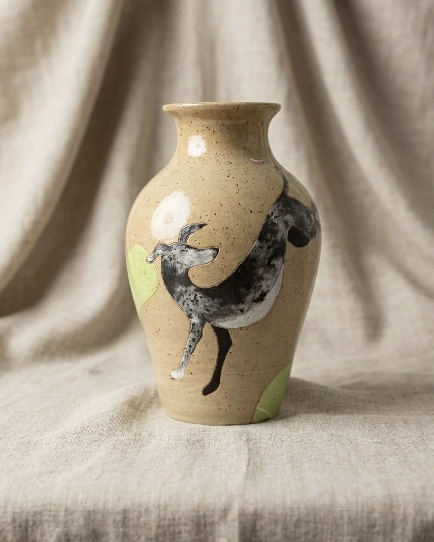A ceramic vase with a painted Dalmatian dog design, set against a beige fabric background.
