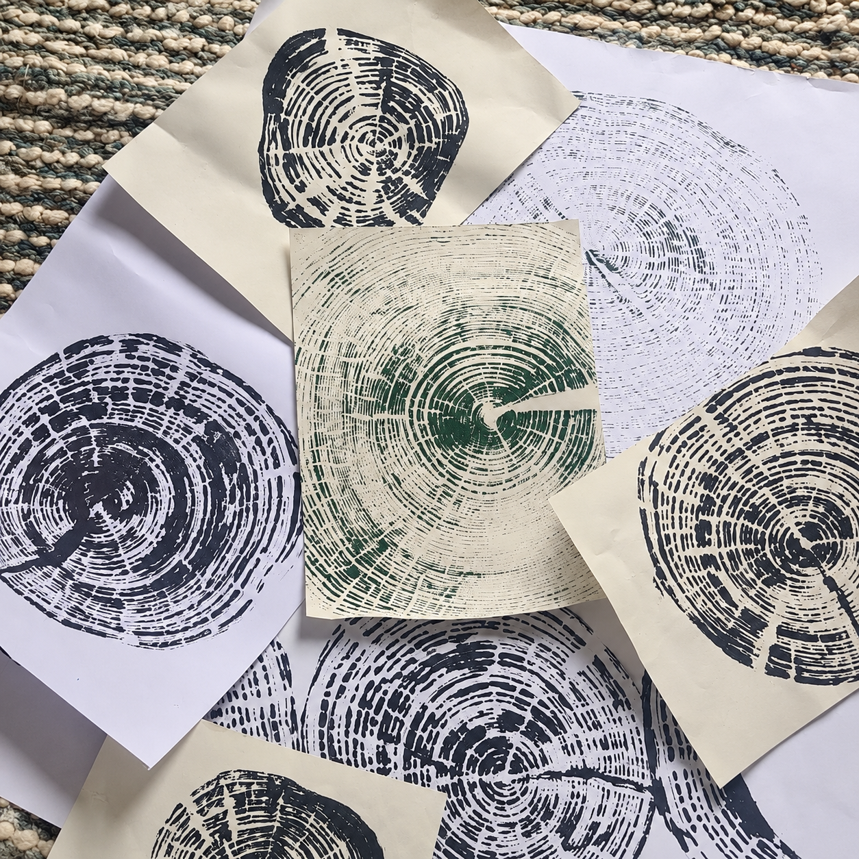 Overlapping art prints featuring circular tree-ring patterns in black, navy, and green ink on paper