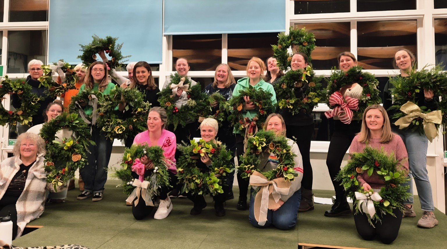 Group of people posing indoors with handmade holiday greenery wreaths and floral arrangements