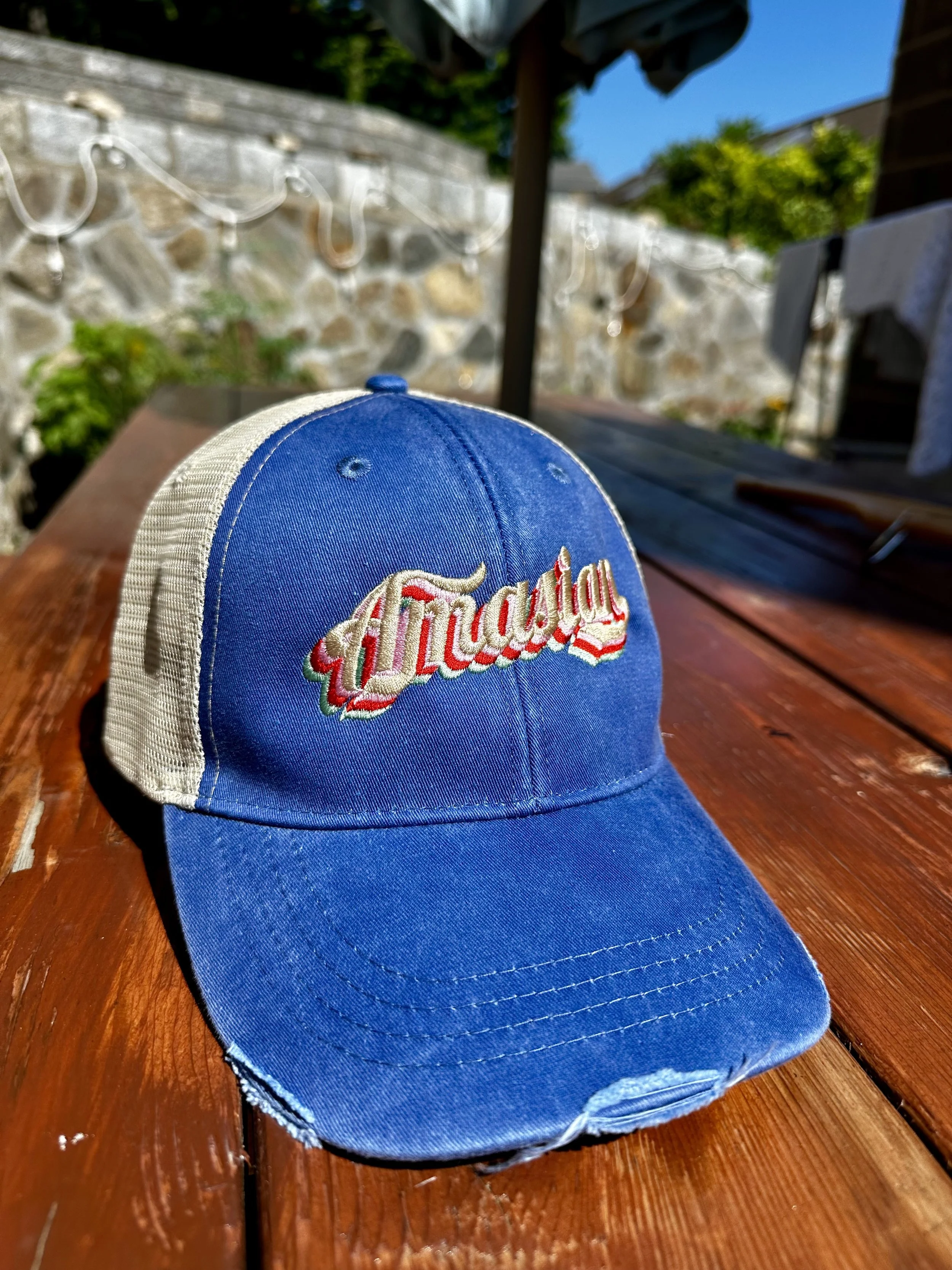 Blue and white baseball cap with red, white, and green embroidered logo on a wooden outdoor table.