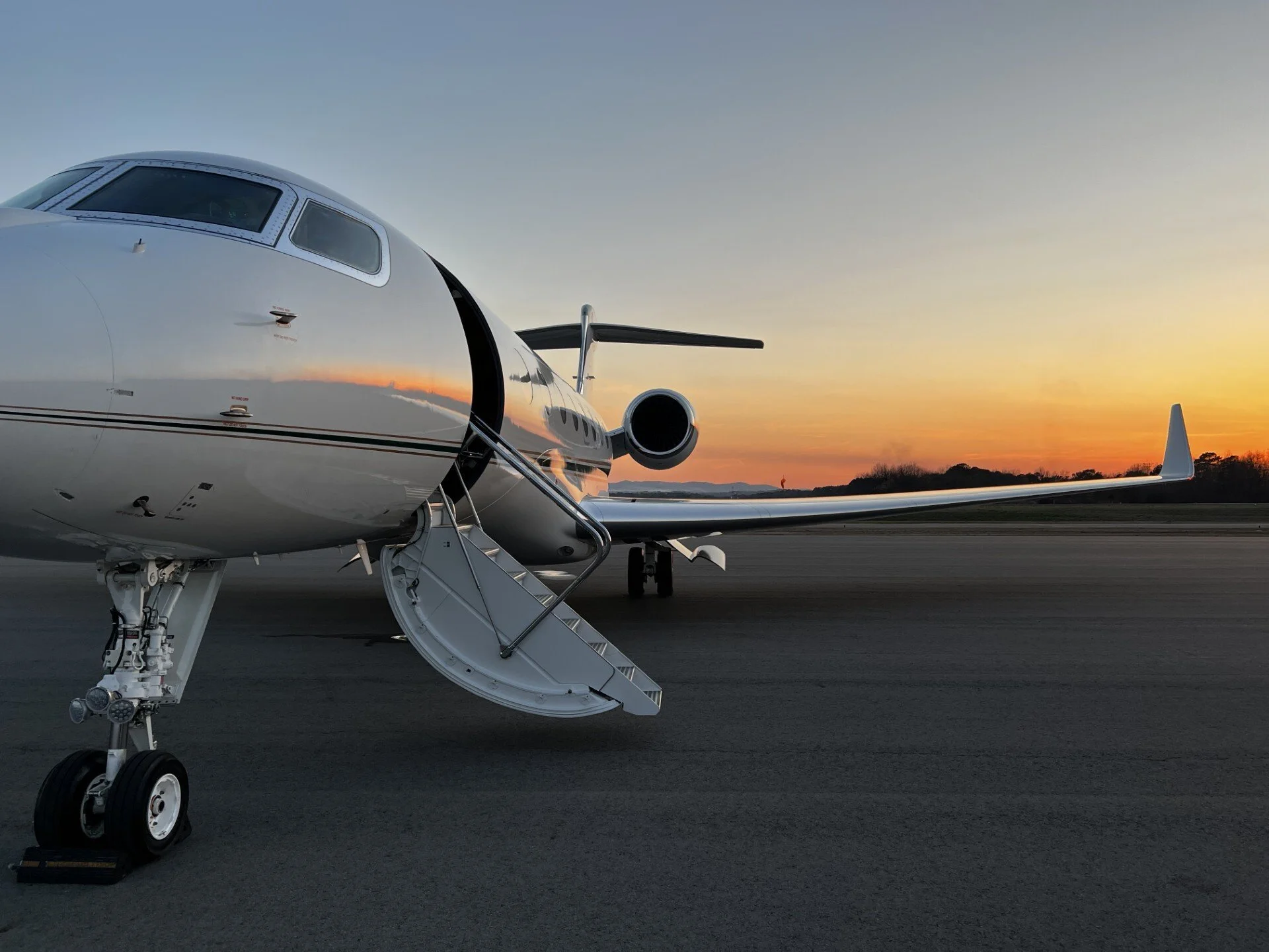 Private jet parked on tarmac at sunset, with stairs extended to the aircraft door.