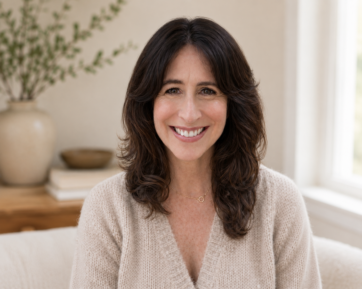 A woman with dark brown, wavy hair smiling in a well-lit room.