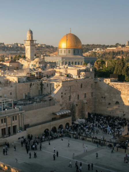 View of the Western Wall Plaza and the Dome of the Rock in Jerusalem, with people praying and visitors in the foreground.