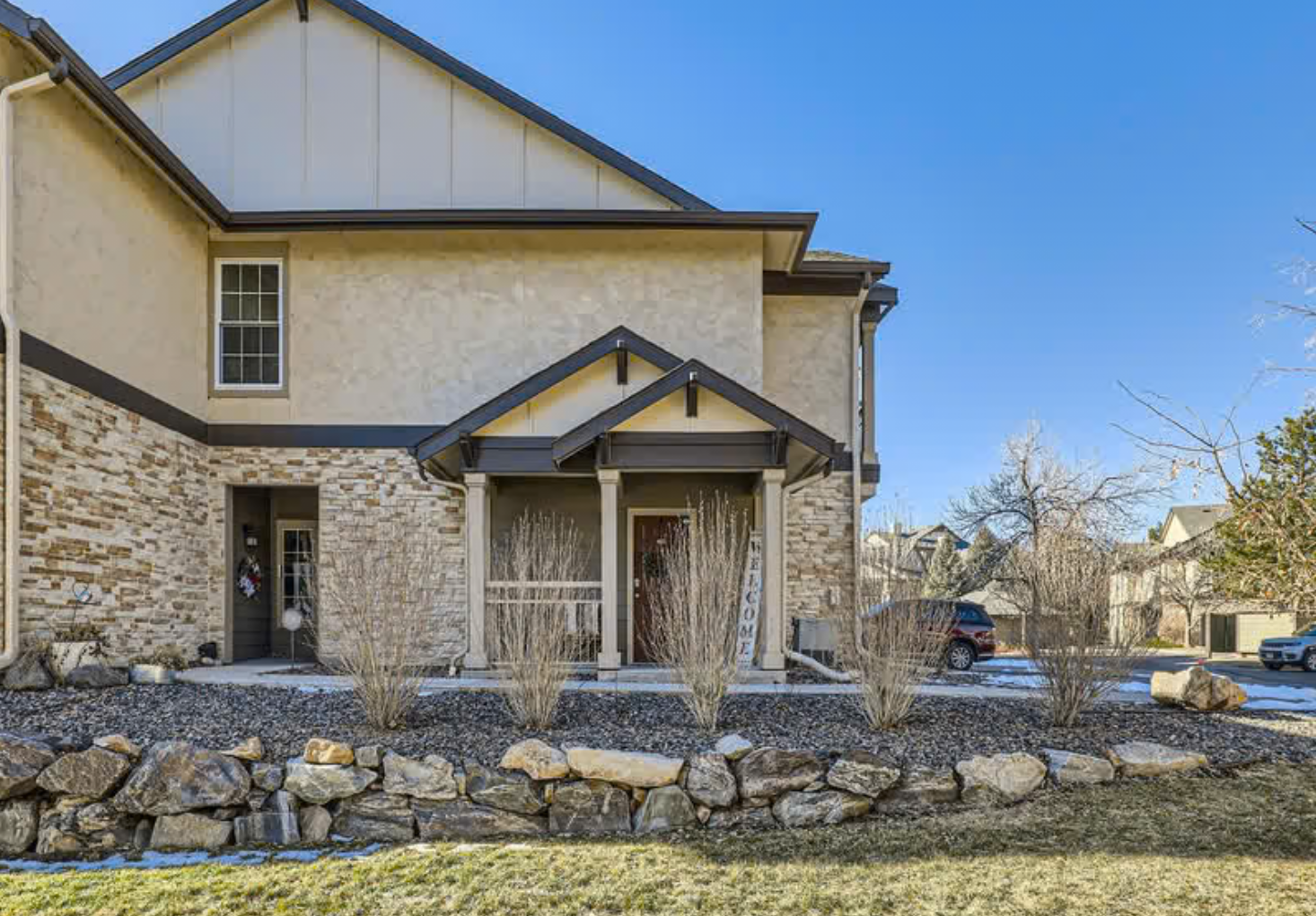 Front view of a modern two-story house with stone and beige siding, a small porch with a