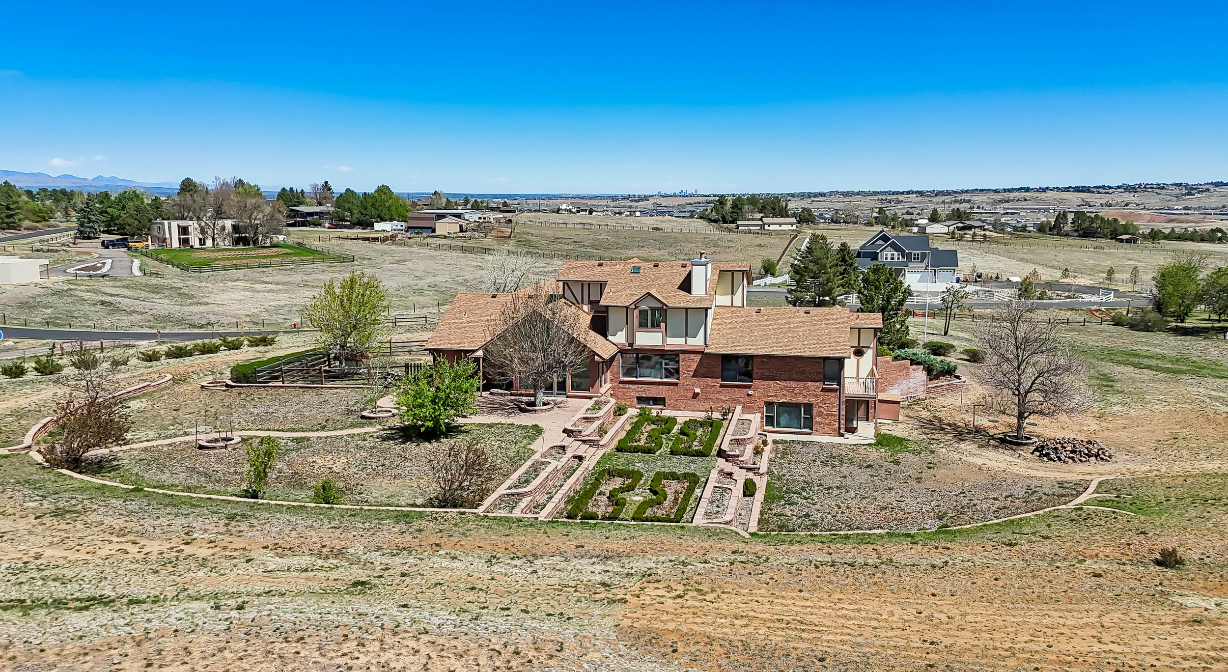 A view of a suburban residential area with a house, landscaped backyard, and distant houses under a blue sky.