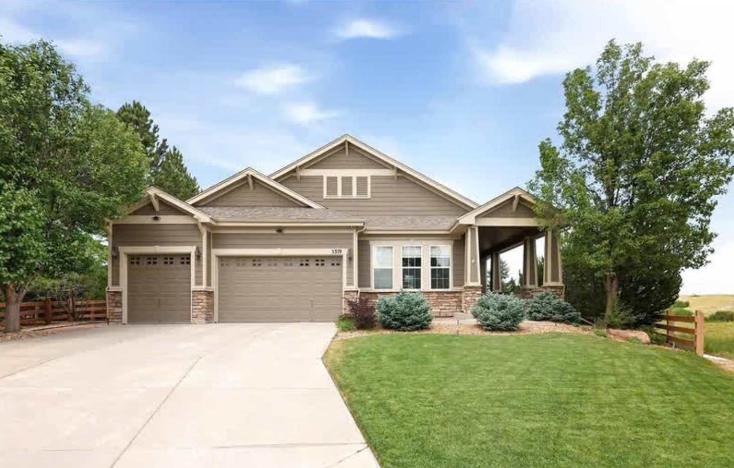 Front view of a modern suburban house with a manicured lawn, two-car garage, and trees on either side.