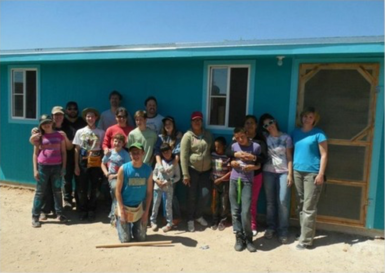 Group of people posing in front of a partially constructed teal building on a sunny day.
