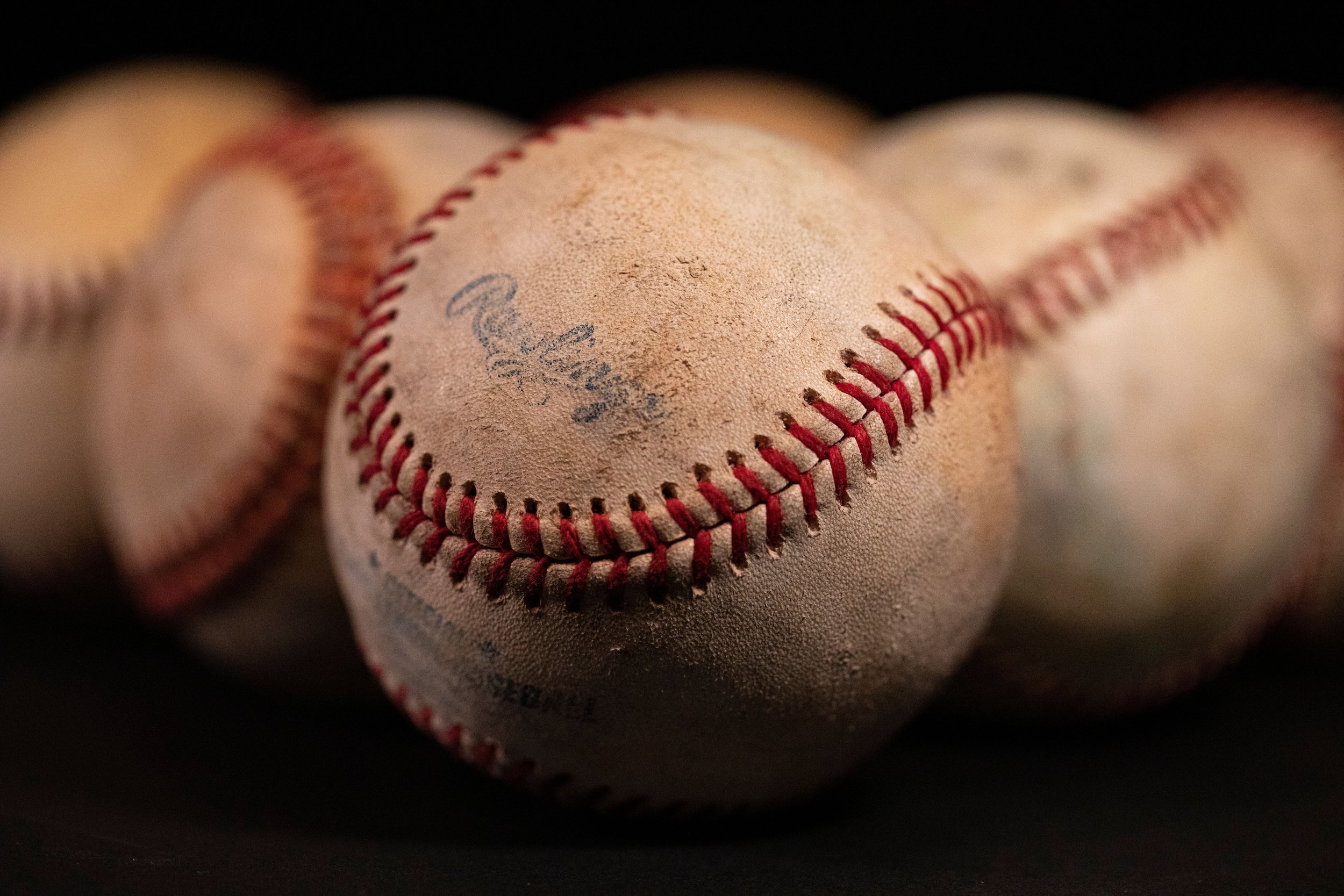 Close-up of a worn baseball with red stitching, focused on the ball's surface showing signs of use and a faded signature or marking.