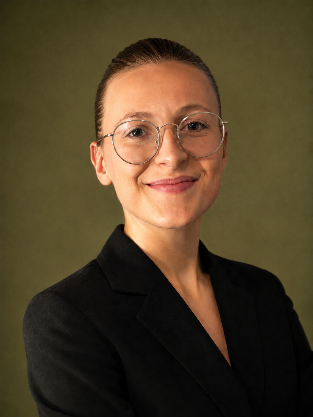 A woman with glasses and a black blazer smiling against a plain green background.