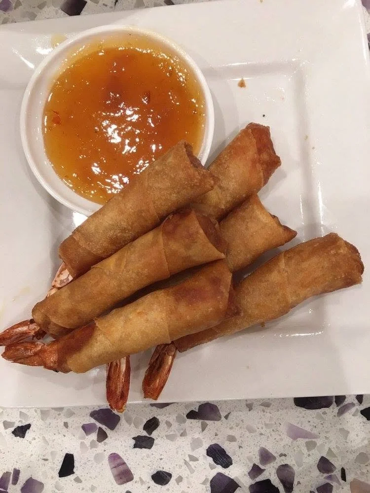 Four shrimp fried spring rolls served with a side of orange dipping sauce on a white square plate