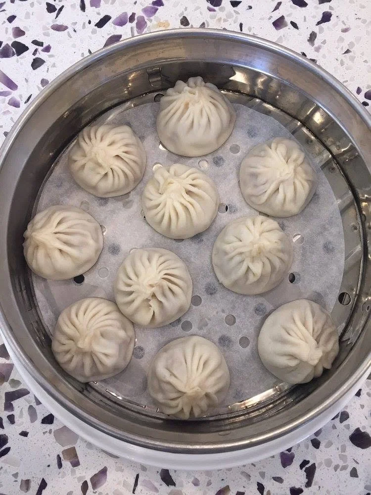 Steamed Chinese soup dumplings, also known as xiaolongbao, in a steamer basket on a speckled countertop.