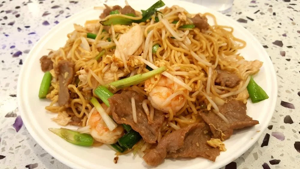 Plate of stir-fried noodles with shrimp, beef, green onions, bean sprouts, and scrambled eggs.