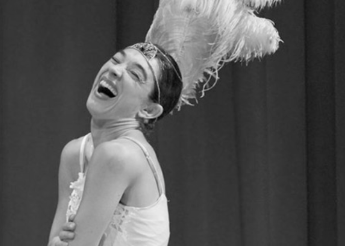 A woman dressed in a costume with a feathered headpiece, laughing joyfully, in a performance setting.