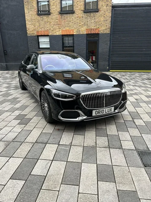 Black luxury Mercedes-Benz car parked on a patterned driveway in front of a brick building with black windows and a large black garage door.