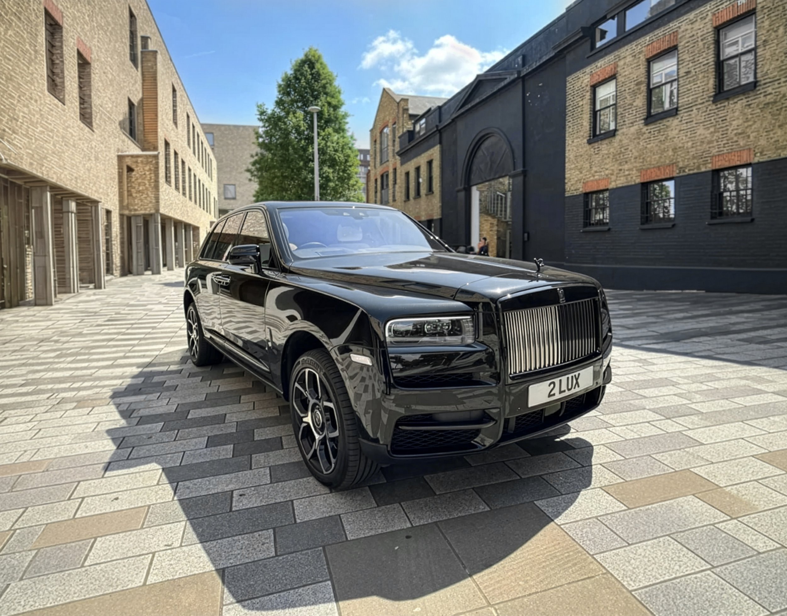 A black luxury Rolls Royce parked on a paved street in front of modern apartment buildings during daylight.