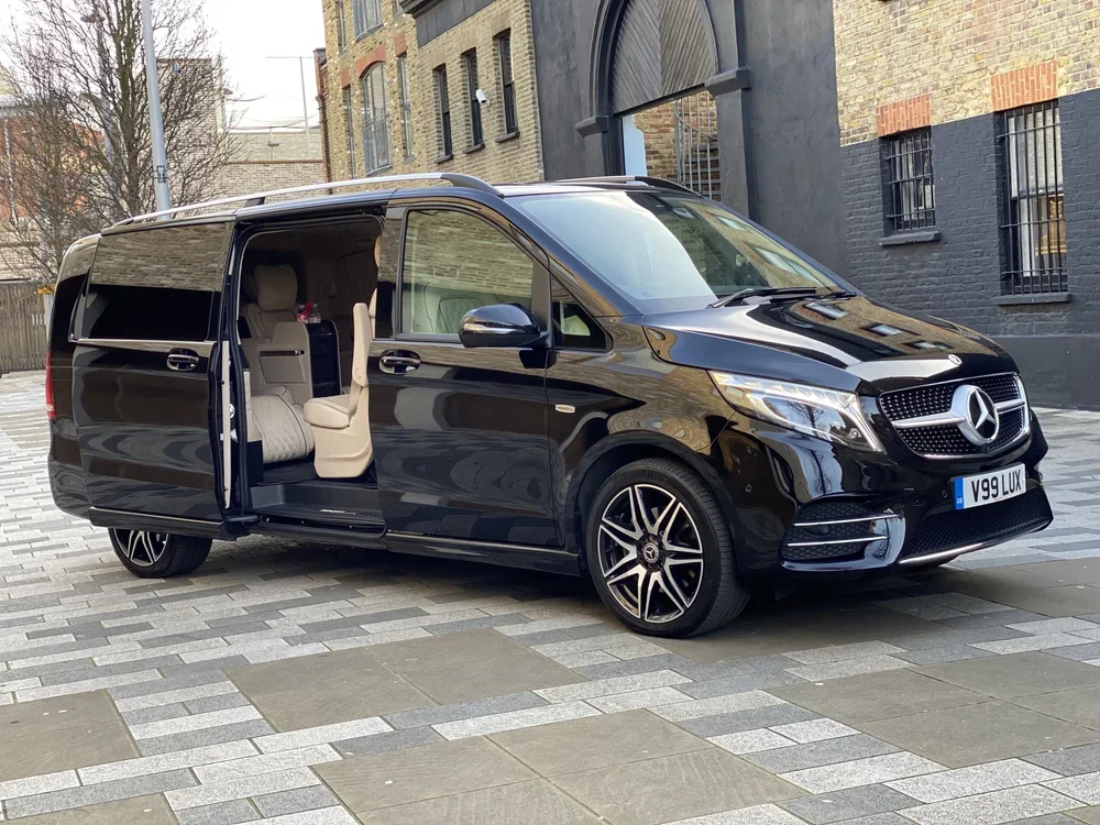 Black Mercedes-Benz van parked on a city street with the sliding door open, revealing beige interior seats.