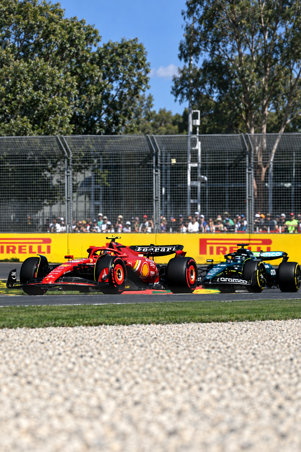 Two Formula 1 race cars, one Ferrari and one Mercedes, racing on a track with a crowd of spectators behind a safety fence, during a sunny day.