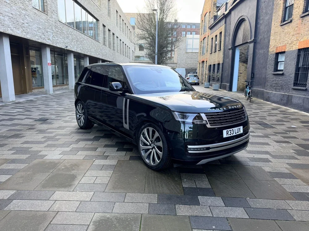 A black Range Rover SUV parked on a brick-paved street in an urban area surrounded by modern buildings.