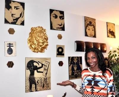 A woman standing in front of a wall decorated with pop art and African-themed artwork, including a gold lion sculpture and a woman in traditional attire.