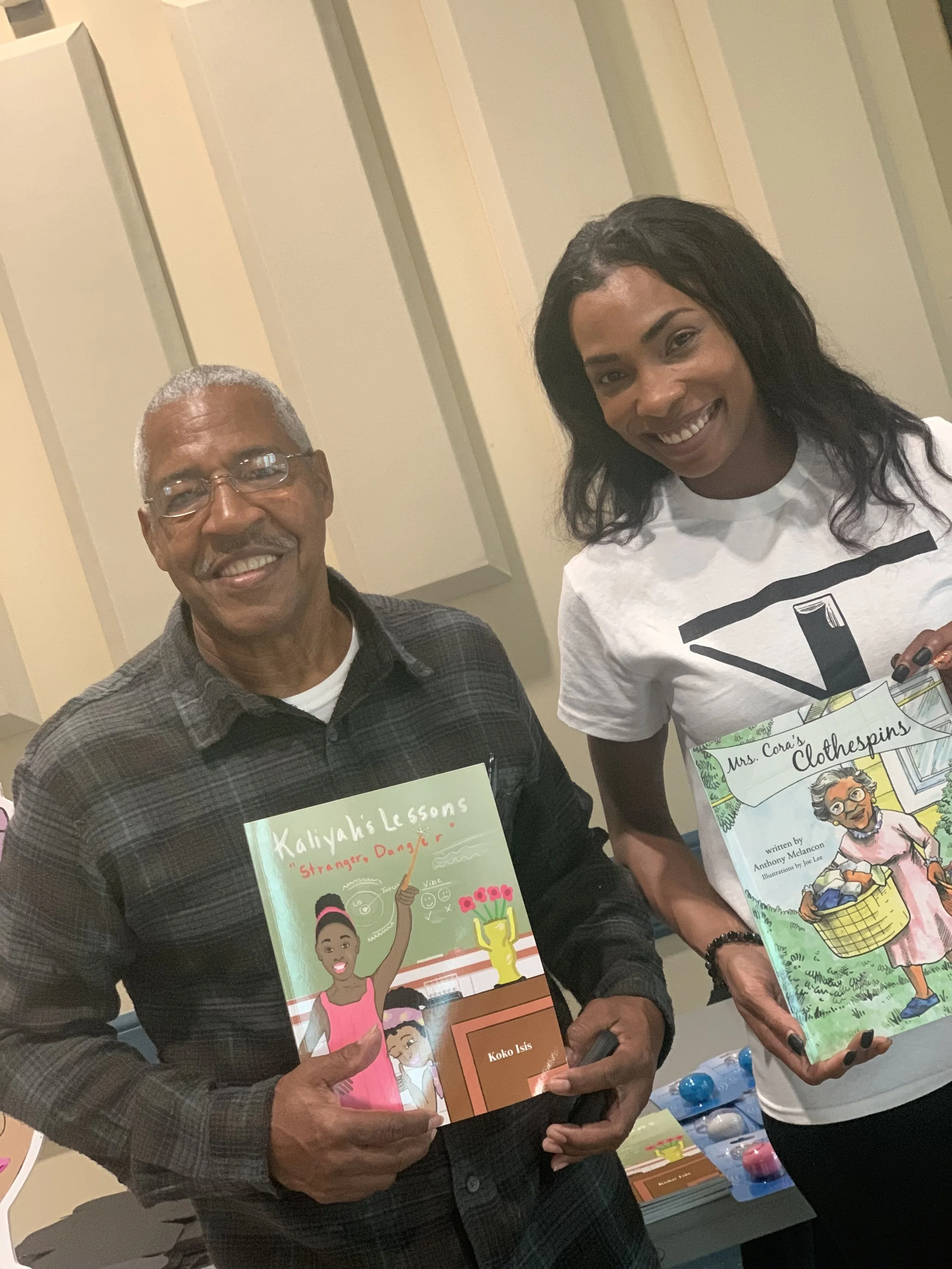 Two smiling women holding colorful children's books at a book event.