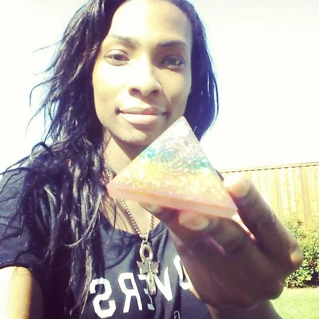 Woman with long dark hair holding a triangular object outdoors, smiling at the camera.
