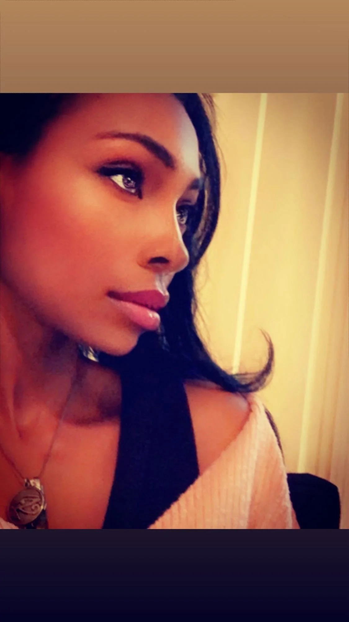 Close-up of a woman with dark hair and makeup, looking to the side, with a soft expression.