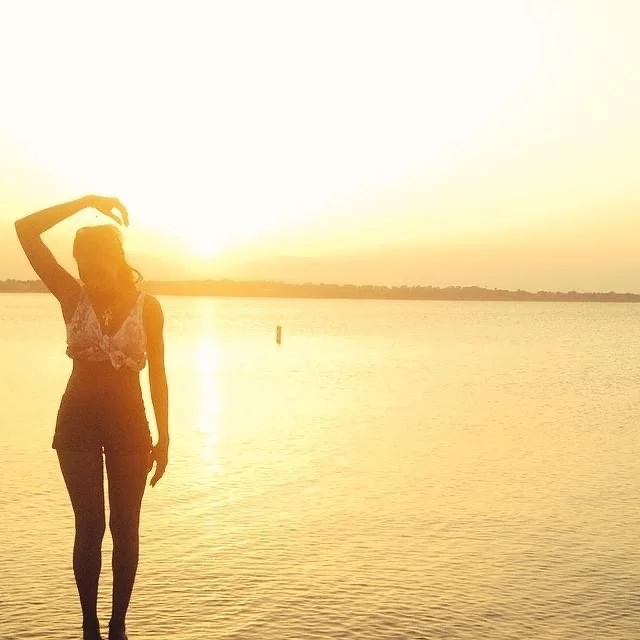 Silhouette of a woman standing by a body of water during sunset.