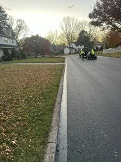 Freshly paved and hot tar of curb lines of a residential street, with houses and trees in the background during daytime