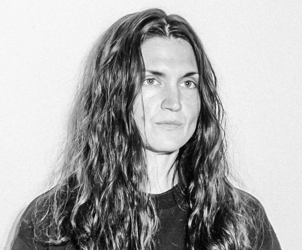 Black and white portrait of a woman with long wavy hair, wearing a dark shirt, looking directly at the camera.