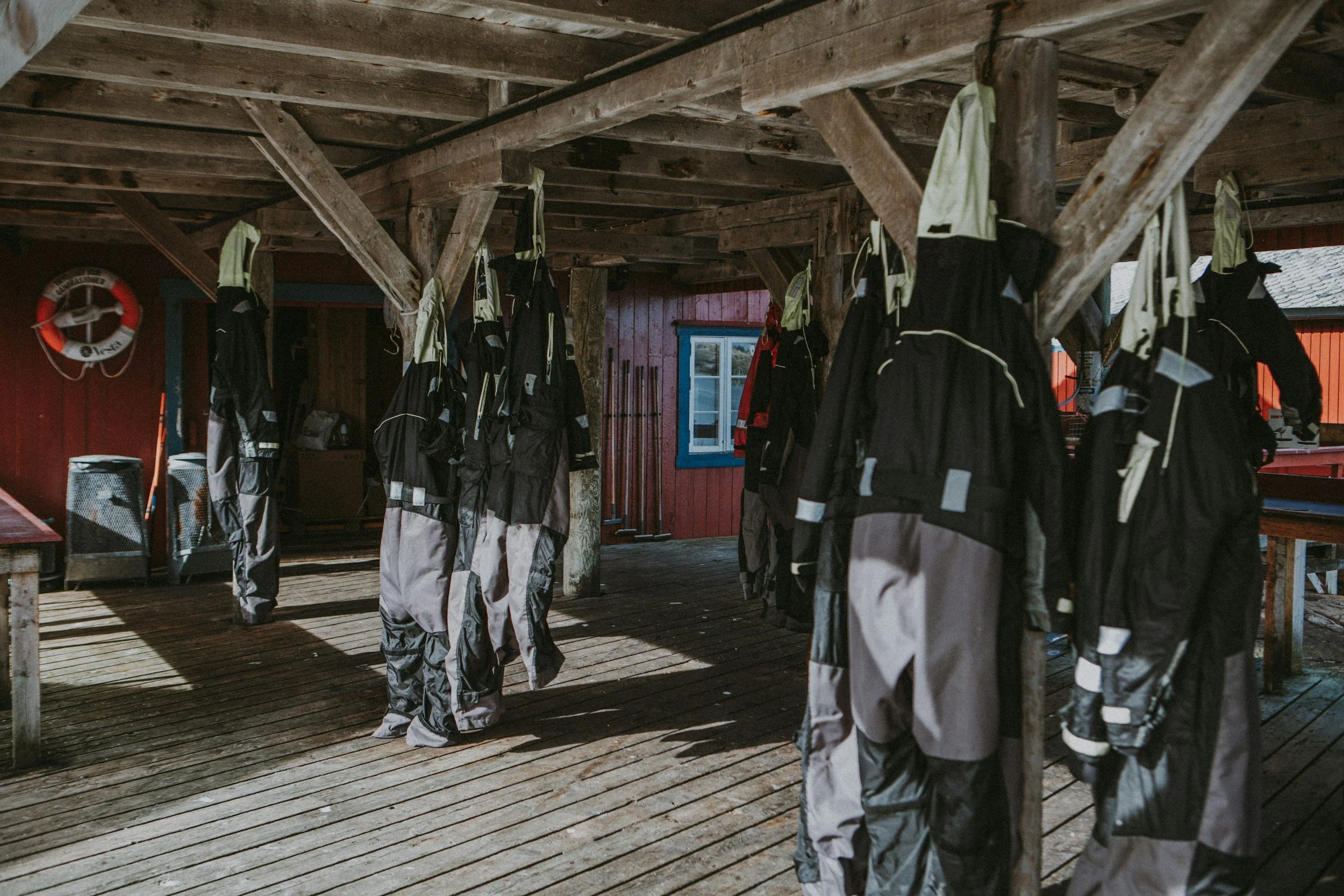 Rows of black and gray jackets hanging from hooks on wooden support beams in a rustic outdoor shed or changing area.