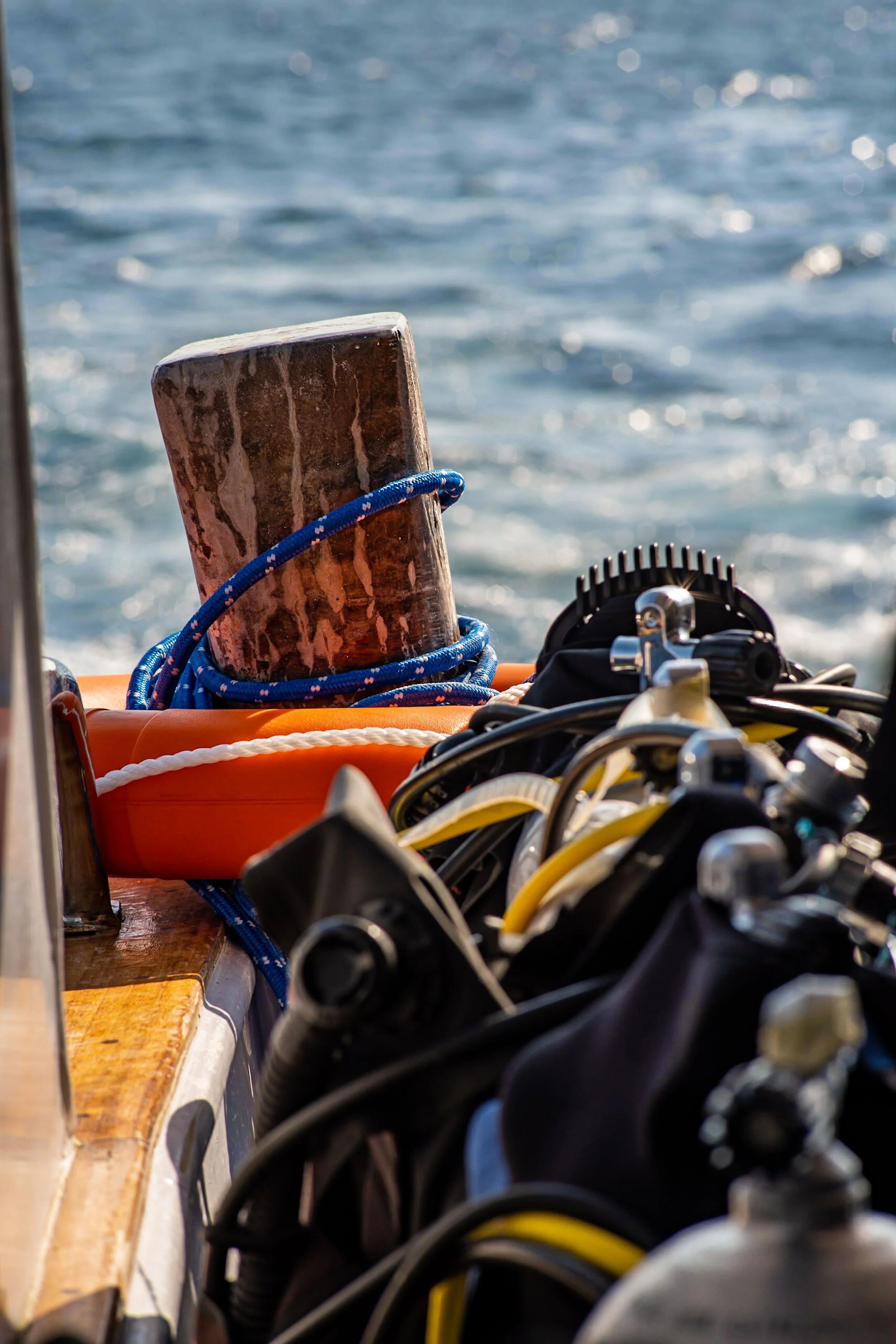 Boat deck with a wooden post, blue ropes, and scattered diving fins against a background of water.