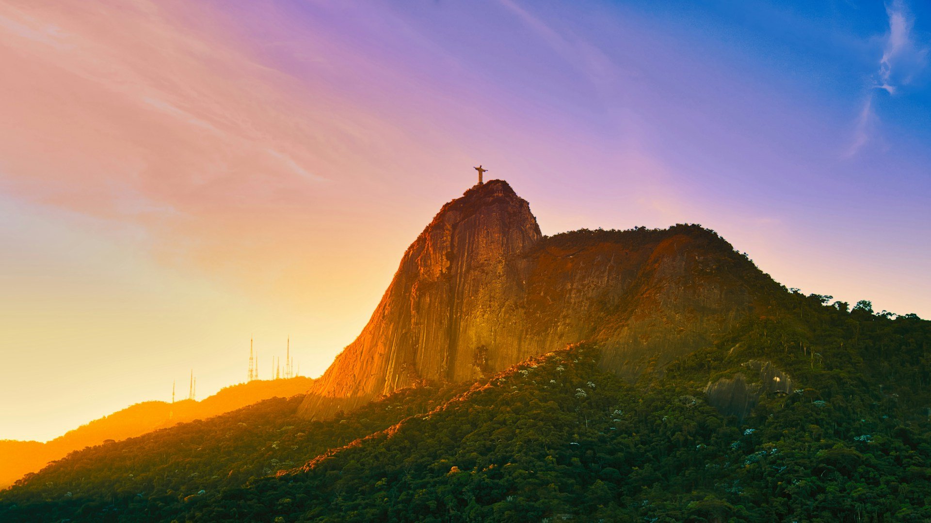 Sunset over the Sugarloaf Mountain in Rio de Janeiro, Brazil, with colorful sky and lush green landscape.