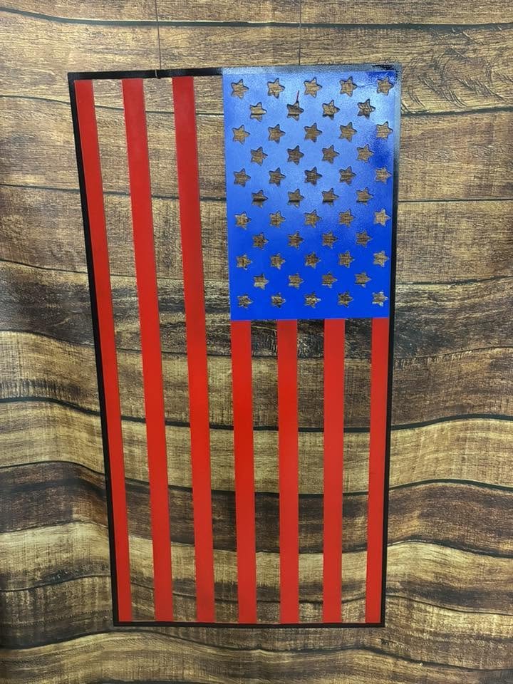 Decorative flag resembling the American flag, with red and black vertical stripes and a blue rectangle with gold stars, mounted on a wooden wall.