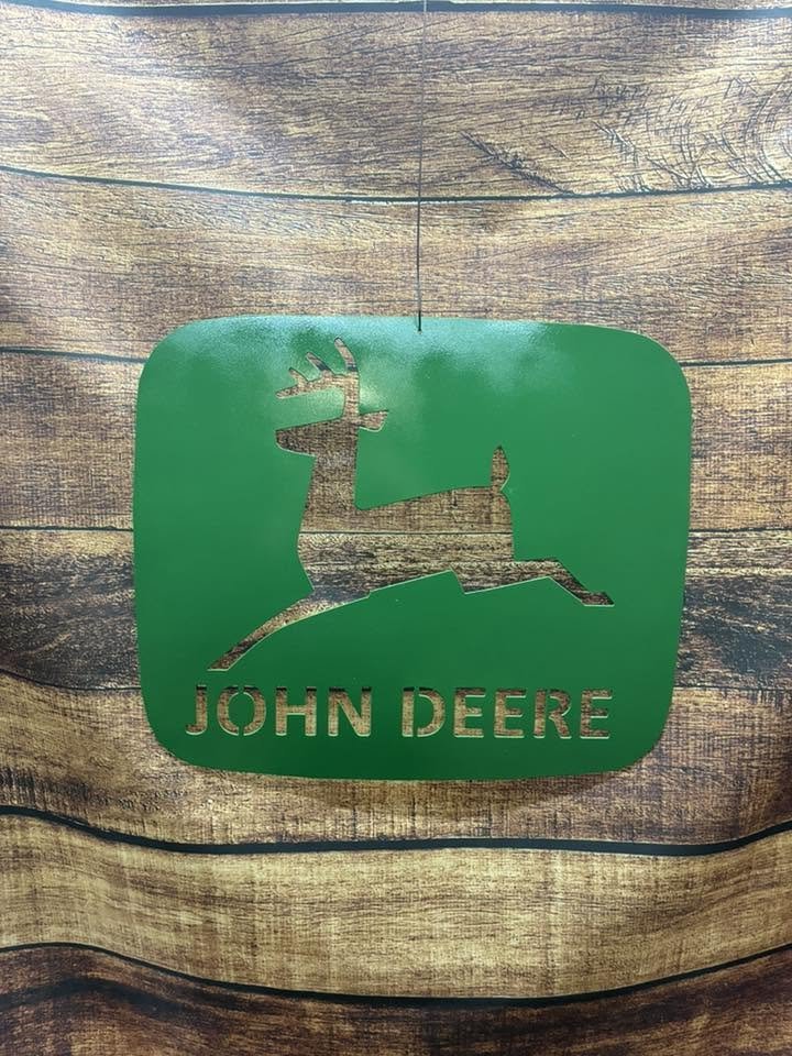Green sign with a cutout of a deer and the words 'John Deere' on a wooden surface.