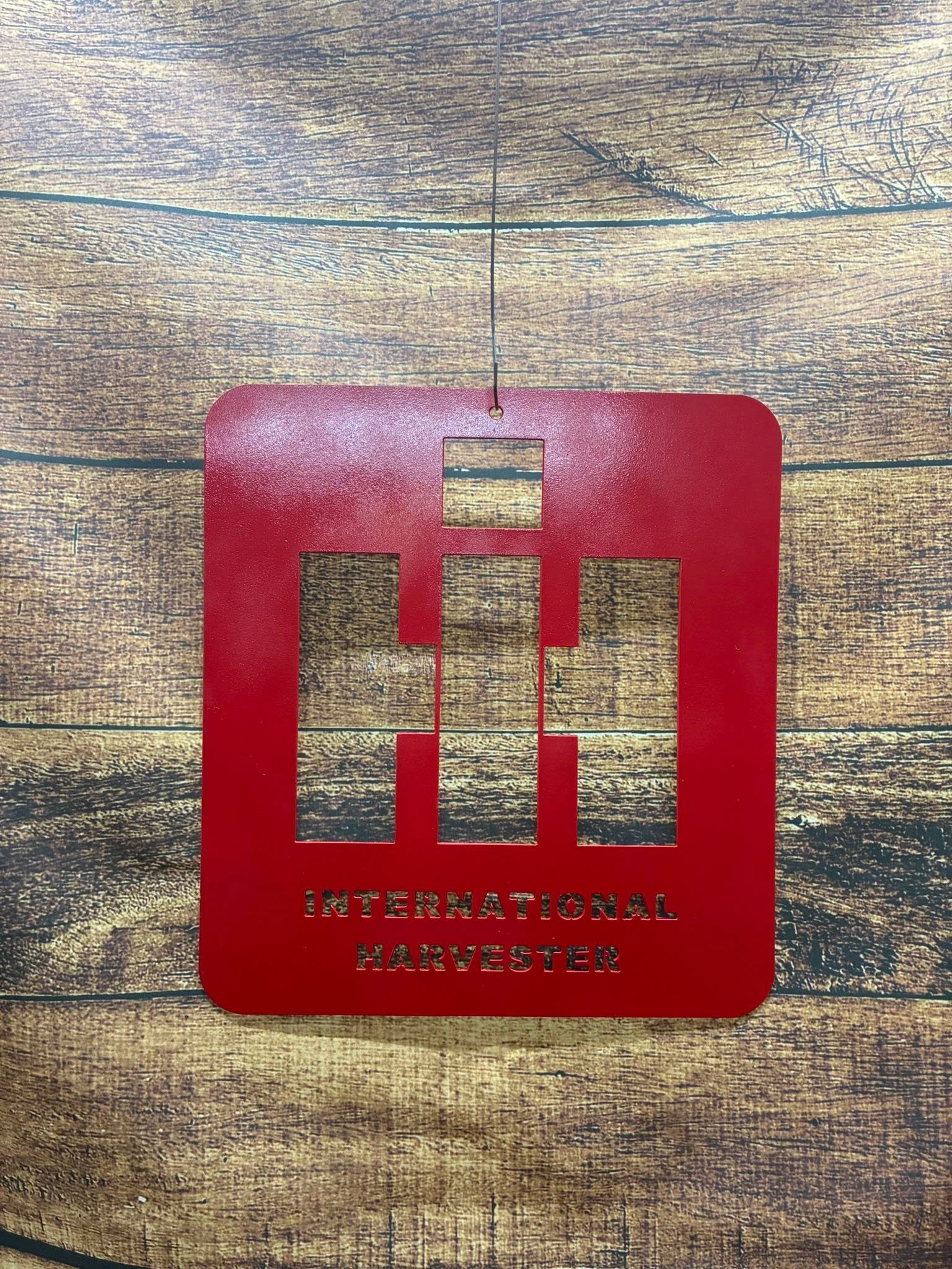 Red metal sign with cutouts spelling 'International Harvester' on a wooden surface.