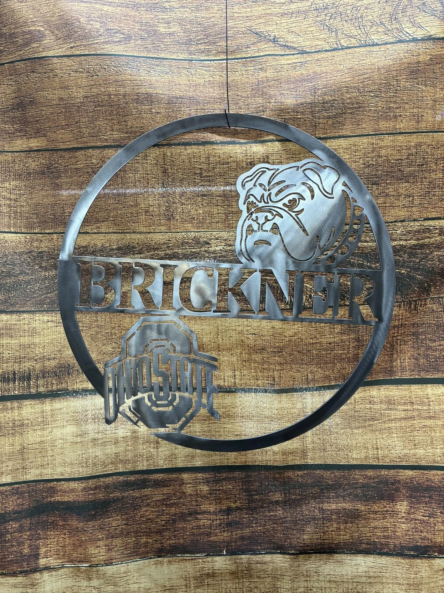 Metal wall decoration featuring a Bulldog face, the word 'BRICKNER', and Ohio State logo, placed on a wooden surface.
